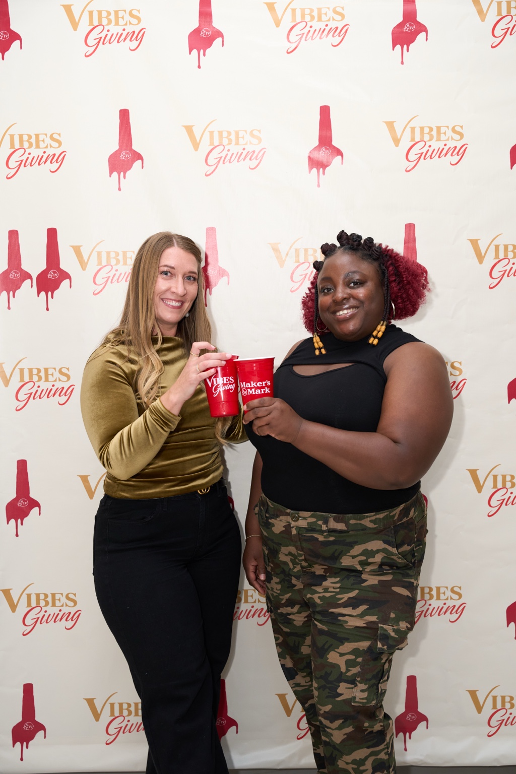Two guests toasting cups in front of the Vibesgiving backdrop